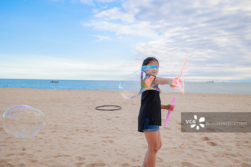 亚洲女孩喜欢在海滩上玩泡泡棒。图片素材