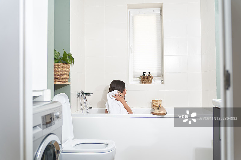 一个女人坐在浴室里的侧影。女孩用白毛巾擦头发图片素材