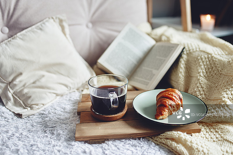一个羊角面包和一杯咖啡在一个舒适的气氛木制托盘。图片素材