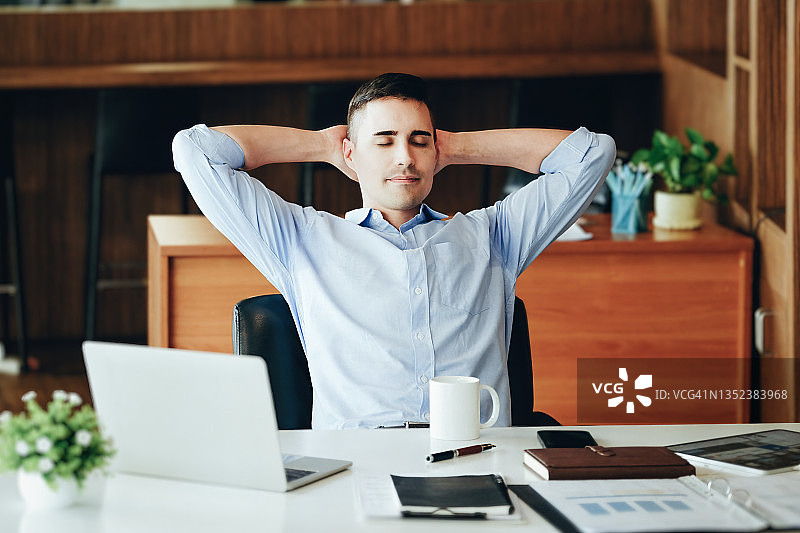 男性营销经理在使用电脑、ipad和营销材料之前，一边工作一边休息、微笑以减少睡意。图片素材