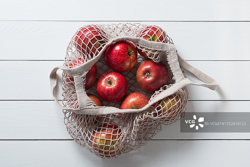 新鲜多汁的有机农场水果，产品在可重复使用的购物袋。苹果装在用回收材料制成的绳袋里，放在白色木桌或背景上。素食主义，纯素食主义，生食。另一种生活方式。没有塑料。副本的空间。新鲜多汁的组织图片素材