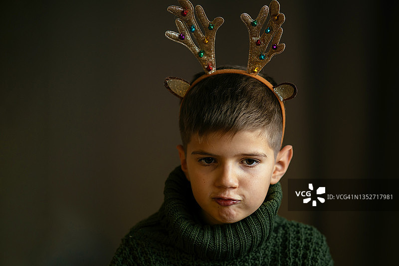 一个穿着绿色毛衣和鹿角的可爱男孩做了个鬼脸图片素材