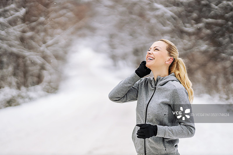 快乐的中年女运动员在冬天站在自然的雪道上打电话。健康生活，通讯，冬季健身图片素材