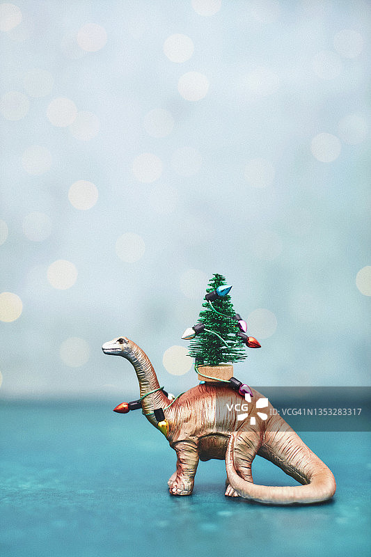 圣诞背景与可爱的金色恐龙携带小圣诞树包裹在节日灯图片素材