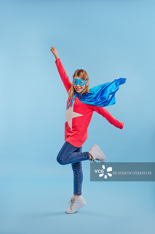 小女孩穿着超级英雄的服装，指着蓝色背景图片素材
