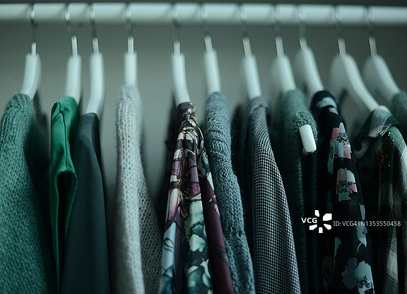 绿色调的衬衫和针织衫排成一行挂在衣架上。在衣柜或衣柜的颜色协调色调的秩序概念图片素材