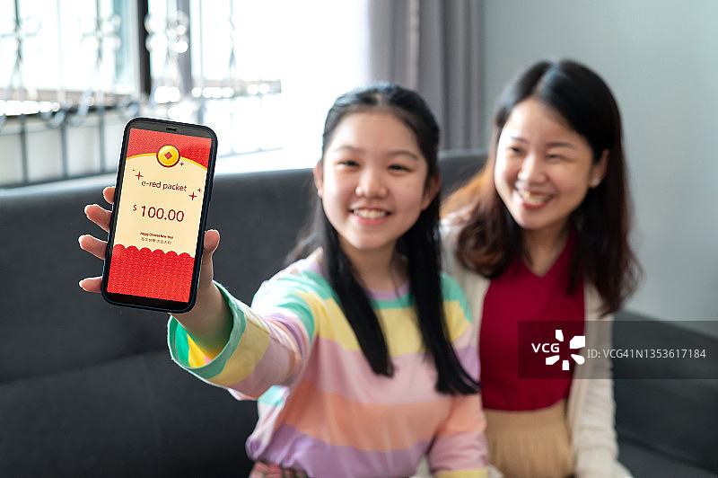 快乐的亚洲少女自豪地展示她的电子红包(数字昂宝)，她从她的母亲通过智能手机。图片素材
