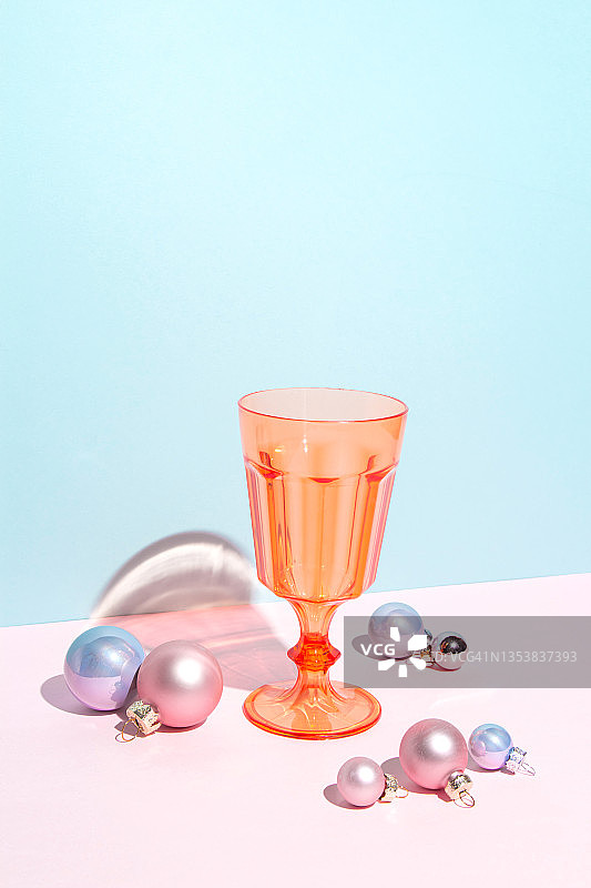 橙色葡萄酒和鸡尾酒杯在蓝色和粉红色的背景与圣诞球。明亮的彩色极简艺术组成。圣诞和新年节日派对的概念。图片素材