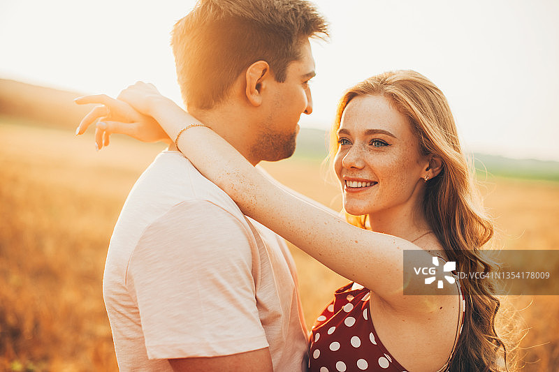 一对夫妇在麦田里拥抱的画像。有雀斑的白种人和男友约会。夕阳光图片素材