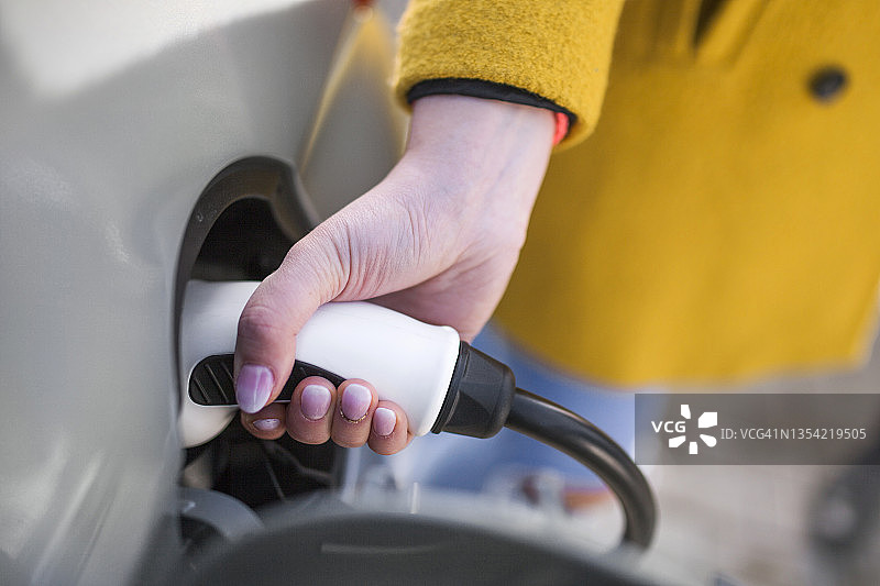 一个年轻女子在停车场给她的电动汽车充电。图片素材