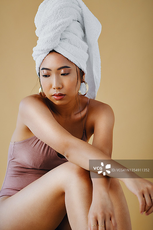 一个迷人的年轻女子独自坐着，看起来很沉思，她的头发用毛巾裹着图片素材