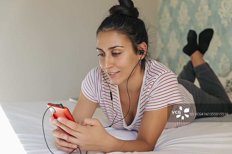 年轻女子戴着耳机使用智能手机在卧室图片素材