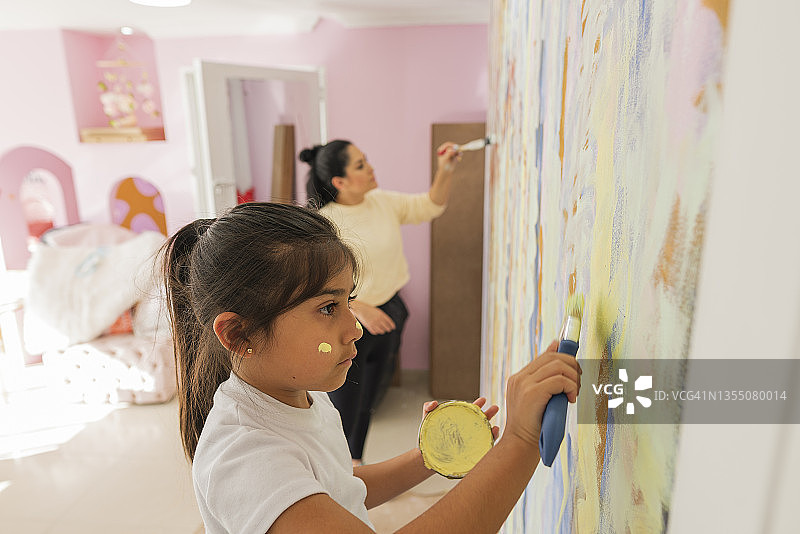 年轻的母亲和她的女儿享受在油漆他们的新房子的墙壁在一个团结和创造力的时刻图片素材