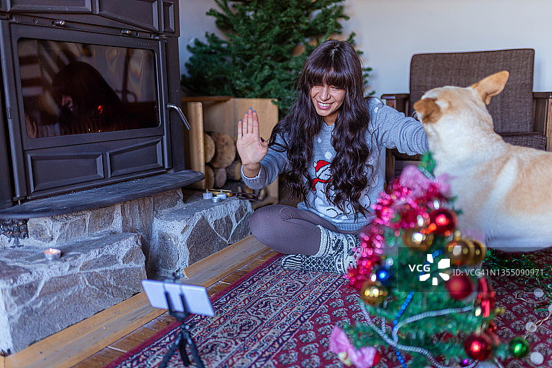 快乐的女人在她的视频通话中挥手，同时装饰她的小圣诞树图片素材