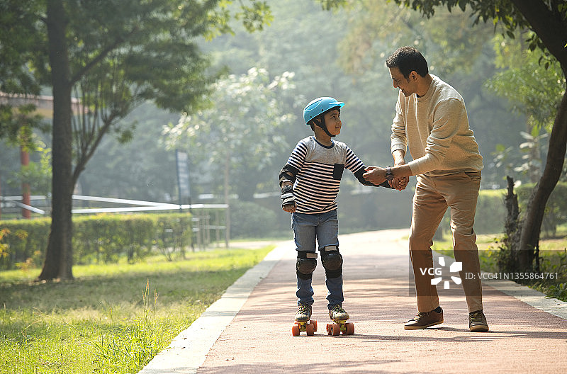 父亲帮助他的儿子在公园滑冰图片素材