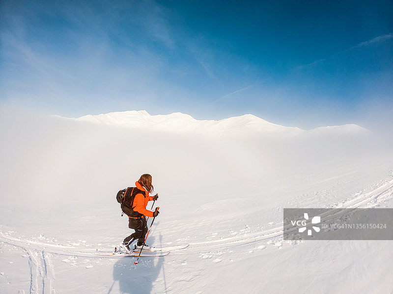 女孩独自用海豹皮沿着一条漂亮的小路向山口滑雪登山图片素材