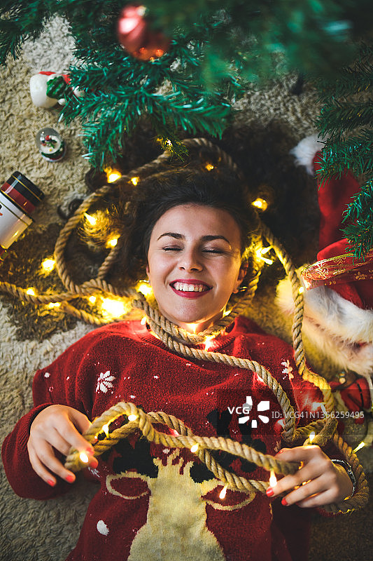 微笑的美女躺在圣诞树下包裹在灯图片素材