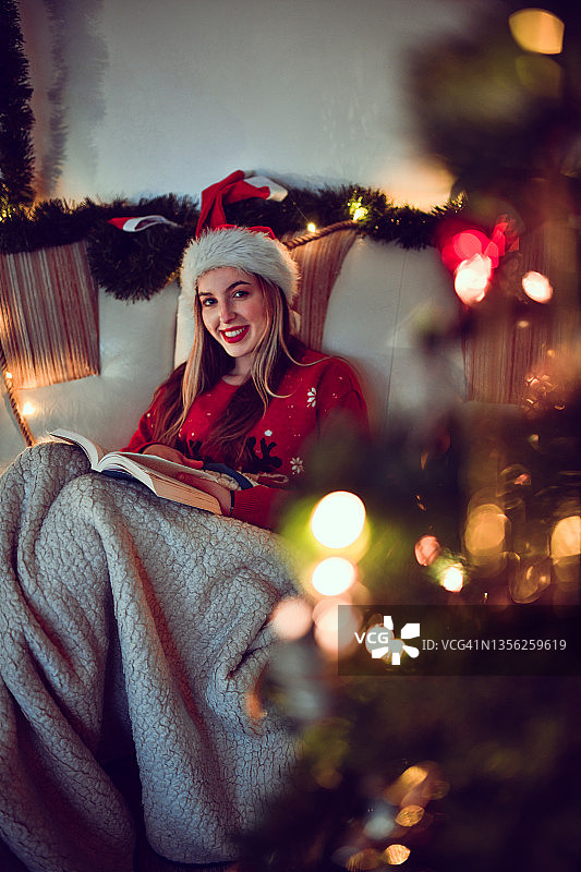 平安夜，戴着圣诞帽，美女在毛毯下享受书图片素材