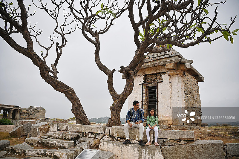 在卡纳塔克邦的罕比，父女俩坐在一座小小的哈努曼神龛和一棵树旁边图片素材