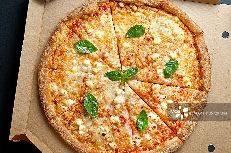 美味的意大利披萨在披萨盒和外卖，在黑色的背景或桌子上。玛格丽塔披萨加番茄和奶酪，切成块，不加肉。素食概念，快餐不健康食品。送货上门或上班。图片素材