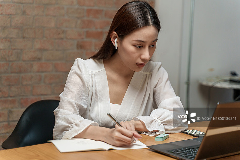 有吸引力的年轻亚洲女学生看着笔记本电脑，同时学习在线课程。图片素材