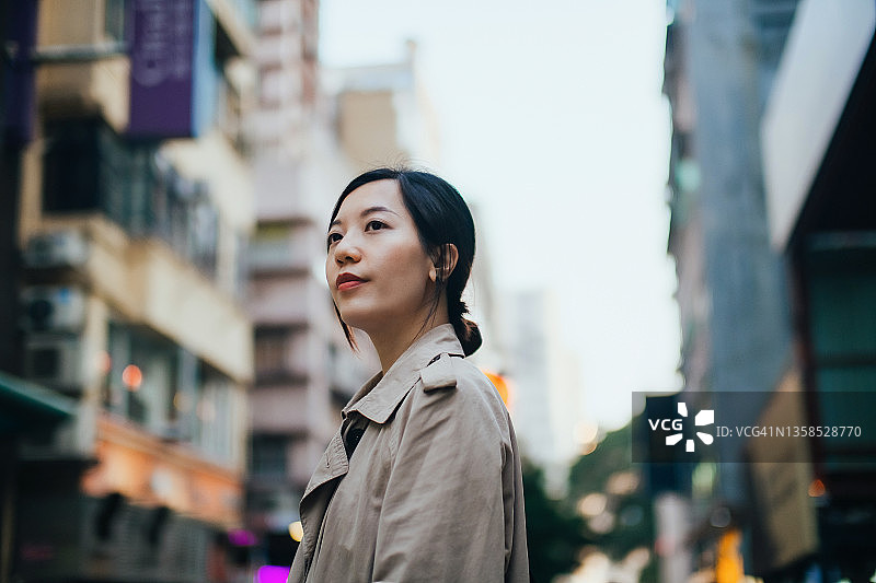 自信的年轻亚洲女商人站在城市街道上看向别处，被高楼大厦包围在城市的中心区。女性领导理念。忙碌的生意图片素材