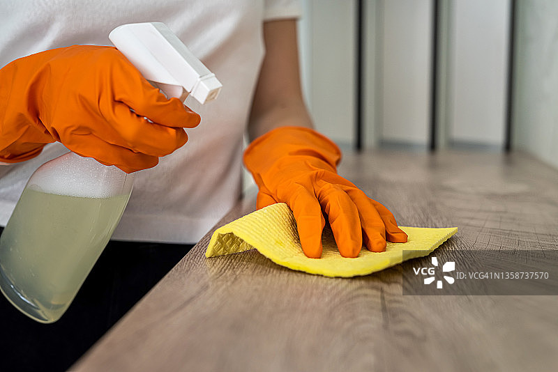 戴着橙色连指手套的美丽女性用手擦拭厨房表面的灰尘图片素材