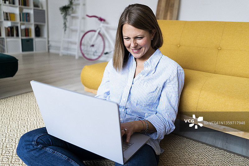 微笑的女人坐在地毯上用笔记本电脑图片素材