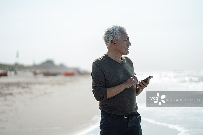 带着智能手机的高级男子站在海滩上图片素材