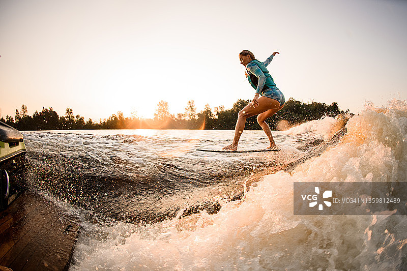 侧视图的女性wakesurfer在巨浪上的wakesurboard上做特技图片素材