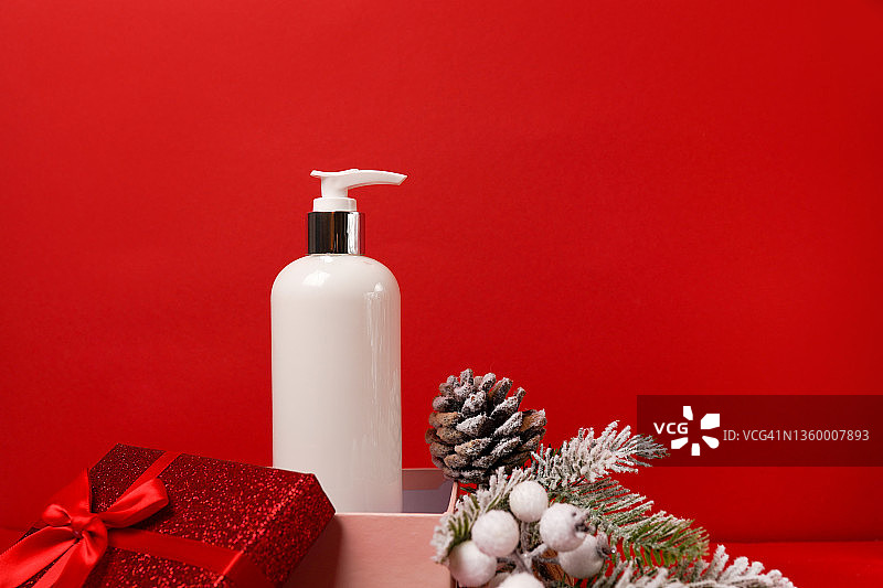 化妆产品乳液或沐浴露在礼品盒上的红色圣诞背景杉树。冬季身体护理产品图片素材