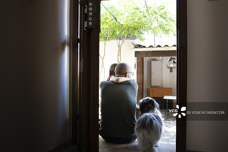在夏日的度假别墅里，父亲和孩子安静地坐在前门的台阶上，由一只小宠物狗看着图片素材