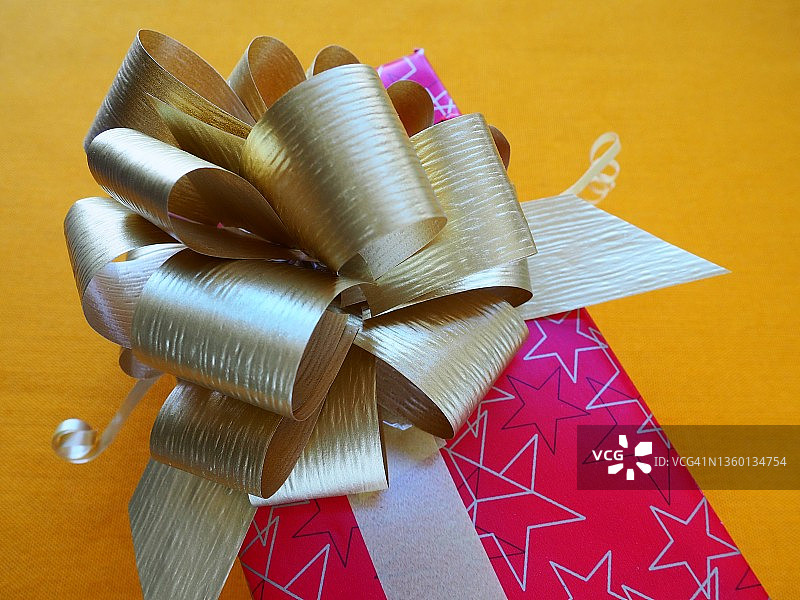 红粉色礼盒，黄色背景上有一个大的金色蝴蝶结。圣诞节，新年，生日，母亲节，婚礼，情人节的礼物。美丽的节日装饰。赠送礼物图片素材