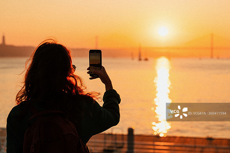 日落时分用智能手机拍水景的女子图片素材