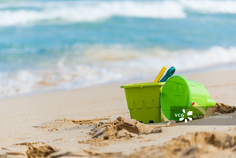 在夏威夷的海滩上，两个带着水桶和铲子的绿色儿童沙玩具的特写镜头图片素材