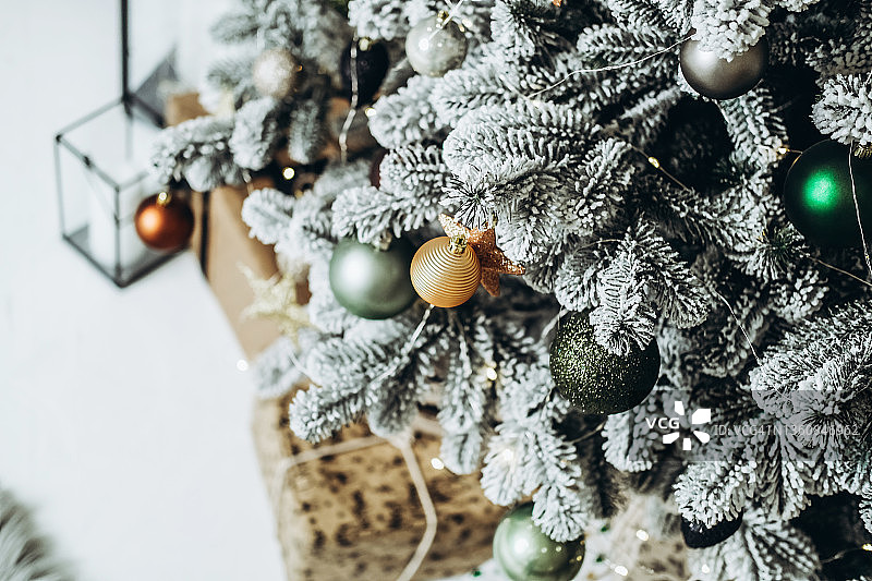 白雪覆盖的圣诞树上有五颜六色的装饰品和礼盒。图片素材