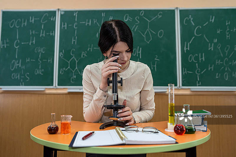 化学年轻的女教师用显微镜坐在书桌前，化学反应图片素材