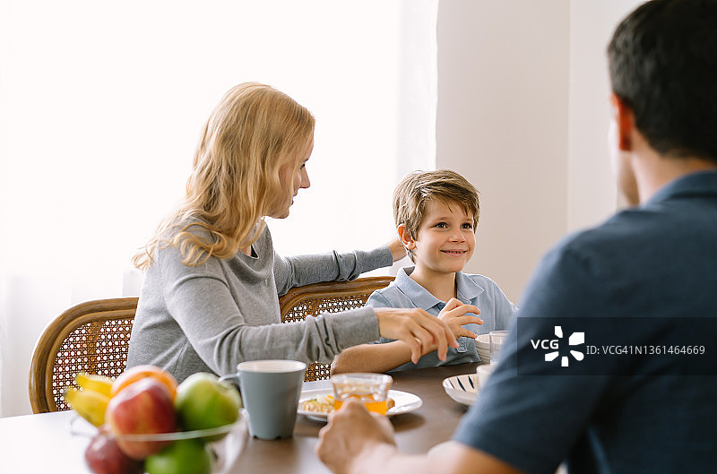 幸福的一家人在家里的桌子上一起吃早餐。大家围坐在一起吃大餐的时候，都用爱的目光看着这个男孩。家庭假日和团聚的概念。图片素材