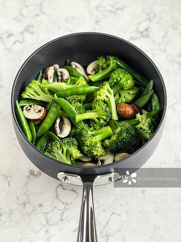在平底锅里蒸蔬菜(花椰菜，甜豌豆)和蘑菇，白色背景图片素材