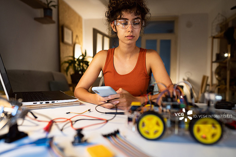 一位女性程序员，工作到深夜，测试她的智能手机控制的、带有传感器的自动驾驶机器人汽车原型图片素材