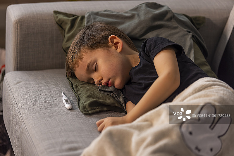 生病的男孩盖着毯子，盖着体温计睡觉。图片素材