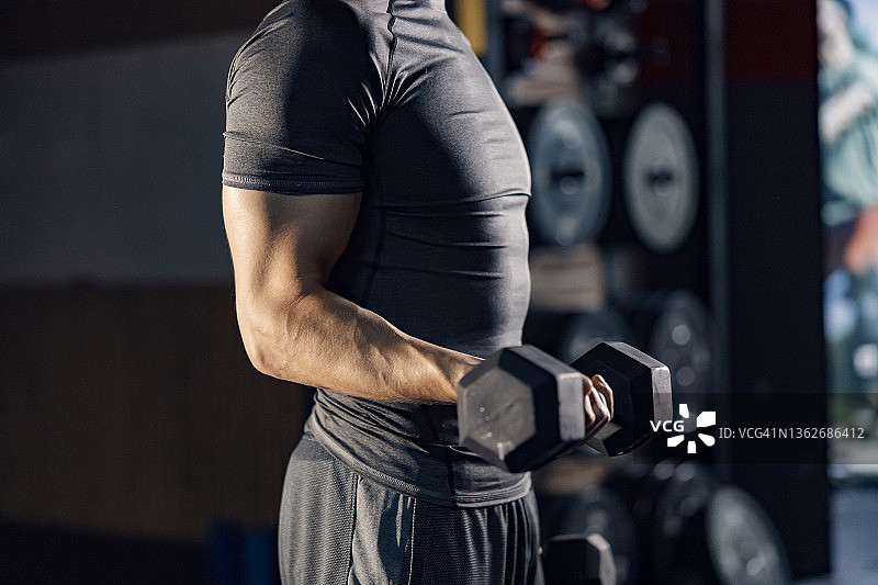 一个不知名的肌肉男在健身房用哑铃锻炼二头肌。图片素材