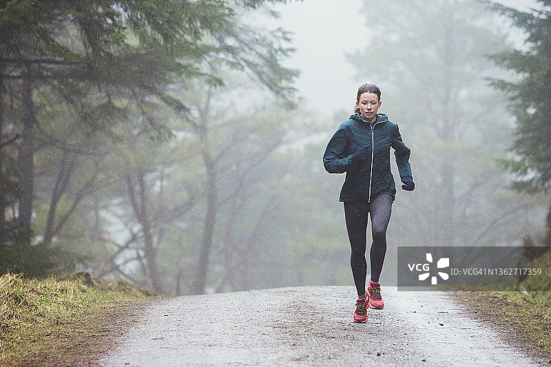 一个专注的女人在雨天的树林里慢跑图片素材