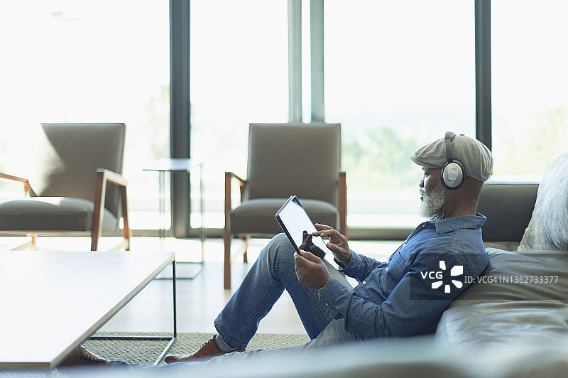 男人放松，在客厅里用耳机和数码平板电脑听音乐图片素材
