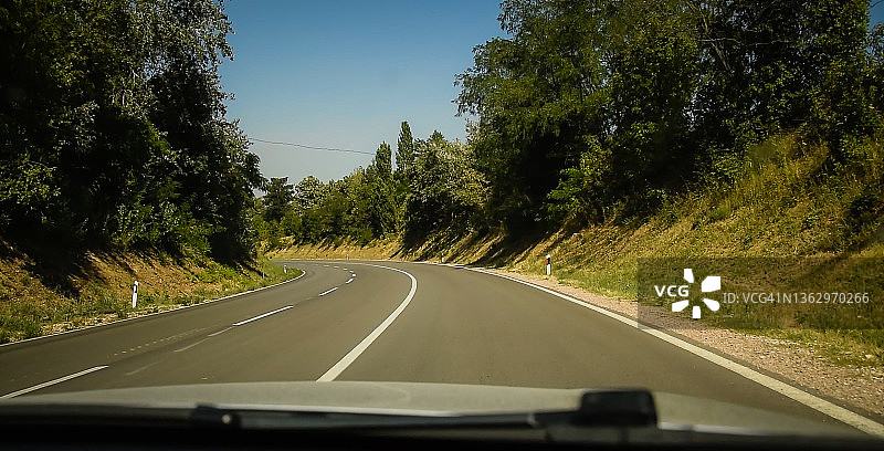在阳光明媚的夏日，宽阔的道路周围是绿色的田野和树木。图片素材