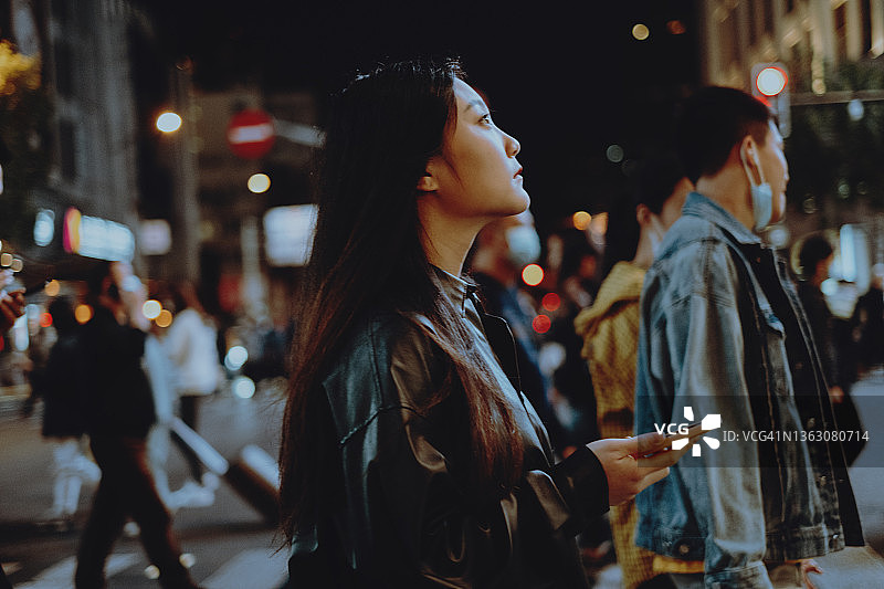 年轻的亚洲女性在城市里用智能手机过马路图片素材