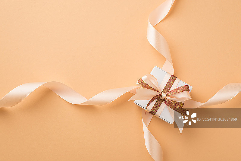顶视图照片的圣瓦伦丁节装饰白色礼品盒与发光的棕色和浅米色丝带蝴蝶结和丝绸卷丝带在孤立的米色背景copyspace图片素材