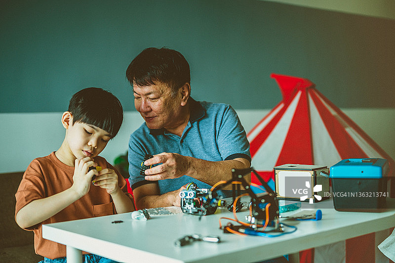 乐观的亚洲爷爷和孙子喜欢他们的机器人爱好图片素材