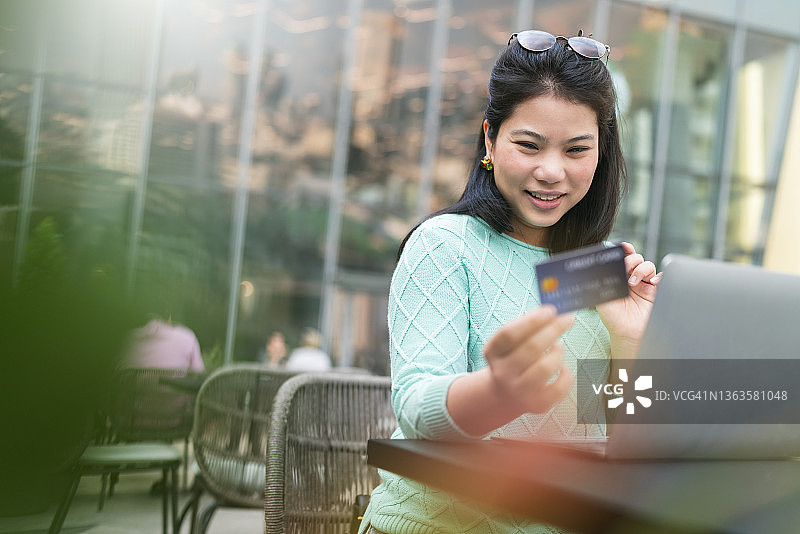有吸引力的成年亚洲女性幸福购物与笔记本电脑，手握信用卡和智能手机购买产品的背景咖啡厅餐厅的经营理念图片素材