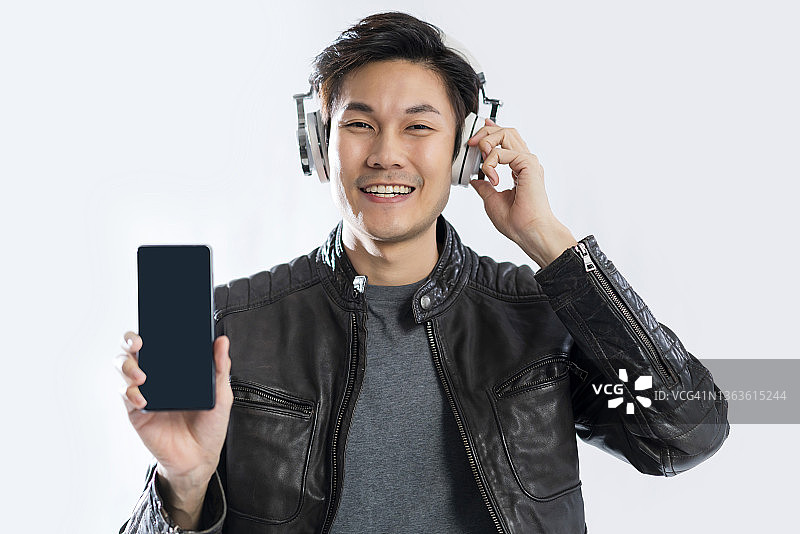 幸福亚洲休闲成熟男人戴耳机音乐播放手势握住显示智能手机黑屏显示为你的文字工作室拍摄白色背景照片微笑的亚洲男性图片素材